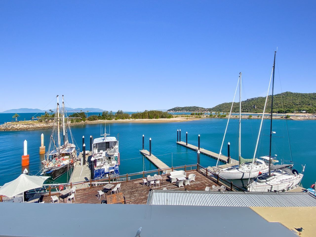 A marina with boats docked, a pier extending into the water, and a clear sky.