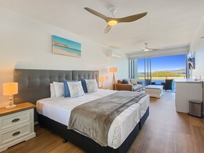 Une chambre avec un grand lit, un ventilateur de plafond, un bureau et une vue sur l’extérieur.