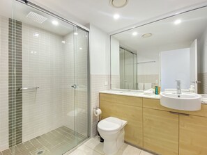 Une salle de bain moderne avec une douche à parois de verre, des toilettes, un lavabo et un miroir.