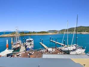 A marina with boats docked, a pier extending into the water, and a clear sky.