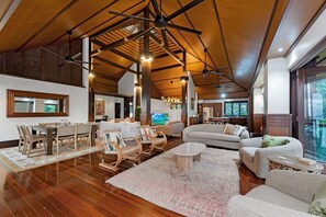 A spacious living area with a high ceiling, wooden beams, and a large window offering a view of the outdoors.