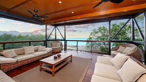 A spacious balcony with wicker furniture, a ceiling fan, and a view of the beach.
