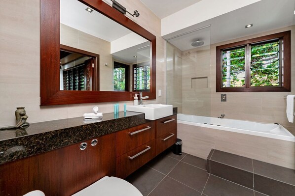 A modern bathroom with a large mirror, a sink, a bathtub, and a window with greenery.