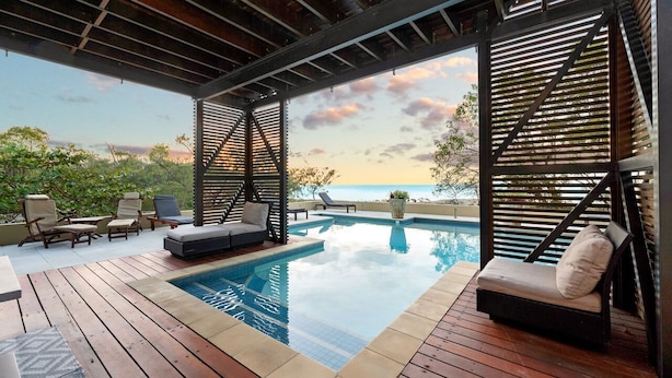 A rooftop pool area with lounge chairs, a hot tub, and a view of the ocean.