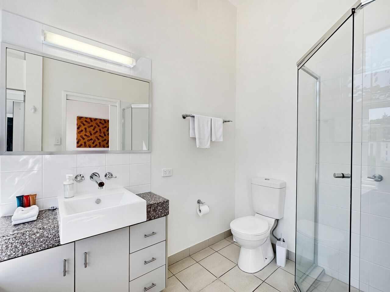 A modern bathroom with a glass shower enclosure, a white sink with a granite countertop, and a toilet.