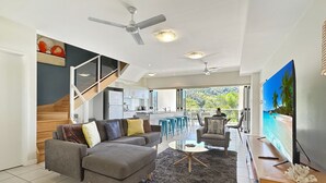 Ein modernes Wohnzimmer mit grauem Sofa, einem Couchtisch und einem Fernseher auf einem Holzboden.