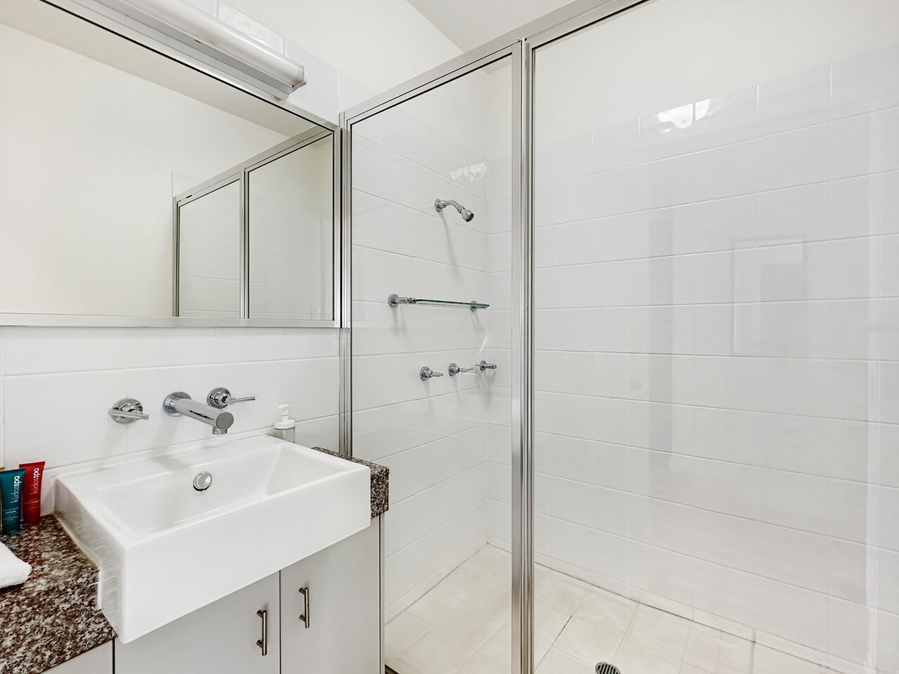 A modern bathroom with a glass shower enclosure, a white sink with a granite countertop, and a mirrored cabinet.