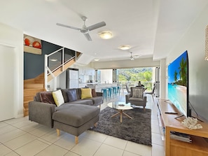 A modern living room with a grey sofa, a coffee table, and a TV on a wooden stand. - Beachside Apartment 14 (Nelly Bay)