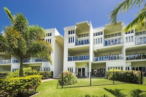 A multi-story hotel with balconies, a well-maintained lawn, and palm trees. - Beachside Apartment 14 (Nelly Bay)