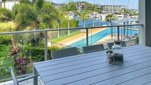 Ein Balkon mit Blick auf einen Hafen, ein Schwimmbad und umliegende Grünflächen.