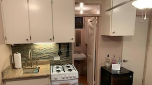 A compact kitchen with white cabinets, a gas stove, a sink, and a black refrigerator.