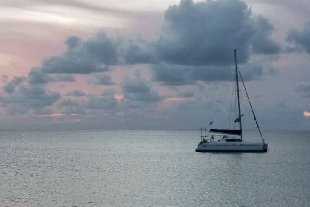 Un voilier sur une eau calme, avec un ciel nuageux en arrière-plan.