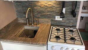 A kitchen with a granite countertop, a sink with a faucet, a stove with four burners, and a backsplash with a stone pattern.