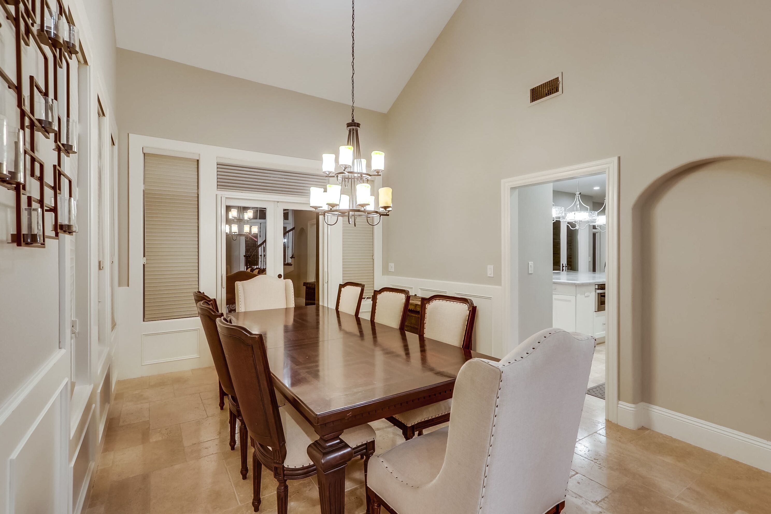 A dining room with a large wooden table, six chairs, and a chandelier.