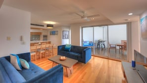 A modern living room with a blue sofa, a coffee table, and a dining area with wooden chairs and a table.