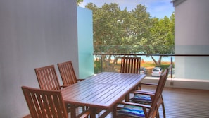 Enjoy a tranquil outdoor space with a table and chairs, overlooking the beach and lush trees.