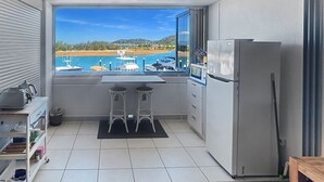 A compact kitchen with a view of a marina, a refrigerator, and a small dining area.