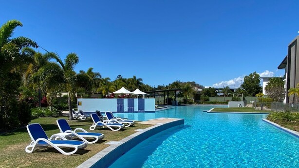 A swimming pool with lounge chairs, a covered area, and a building in the background.
