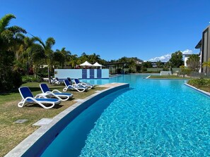 Una piscina con sillas de descanso, un área techada y un edificio al fondo.