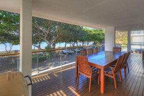 A wooden deck with a table and chairs, overlooking a road and trees.