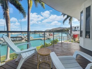 Een balkon met witte loungestoelen, een rieten tafeltje en uitzicht op een jachthaven met boten en een steiger.