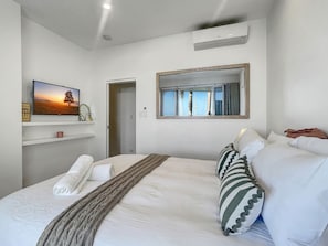 Hotellihuone, jossa on suuri sänky, taulutelevisio, peili ja ikkuna, josta avautuu näkymä palmuille.