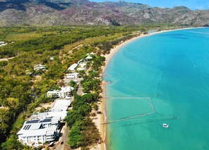 An aerial view of a coastal area with a beach, buildings, and clear blue water.