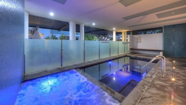 A modern indoor pool with glass walls, a hot tub, and a tiled floor.