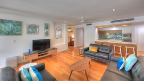 A modern living room with a flat-screen TV, two sofas, a coffee table, and a kitchen area with a bar counter.