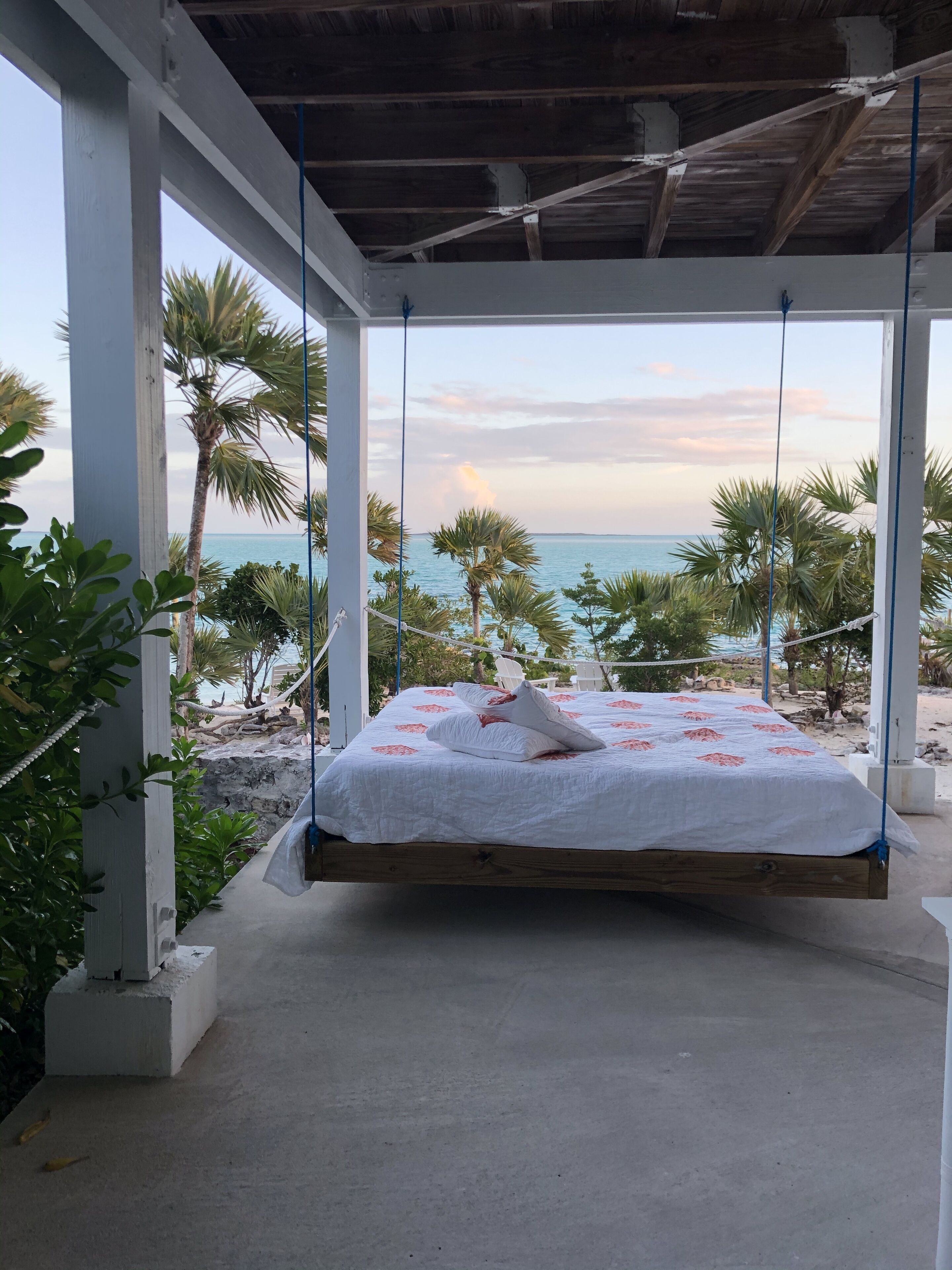 Una cama suspendida en una estructura blanca, con vista al mar y palmeras.