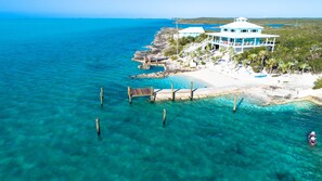A coastal property with a white sandy beach, clear turquoise water, and a large house with a blue roof.