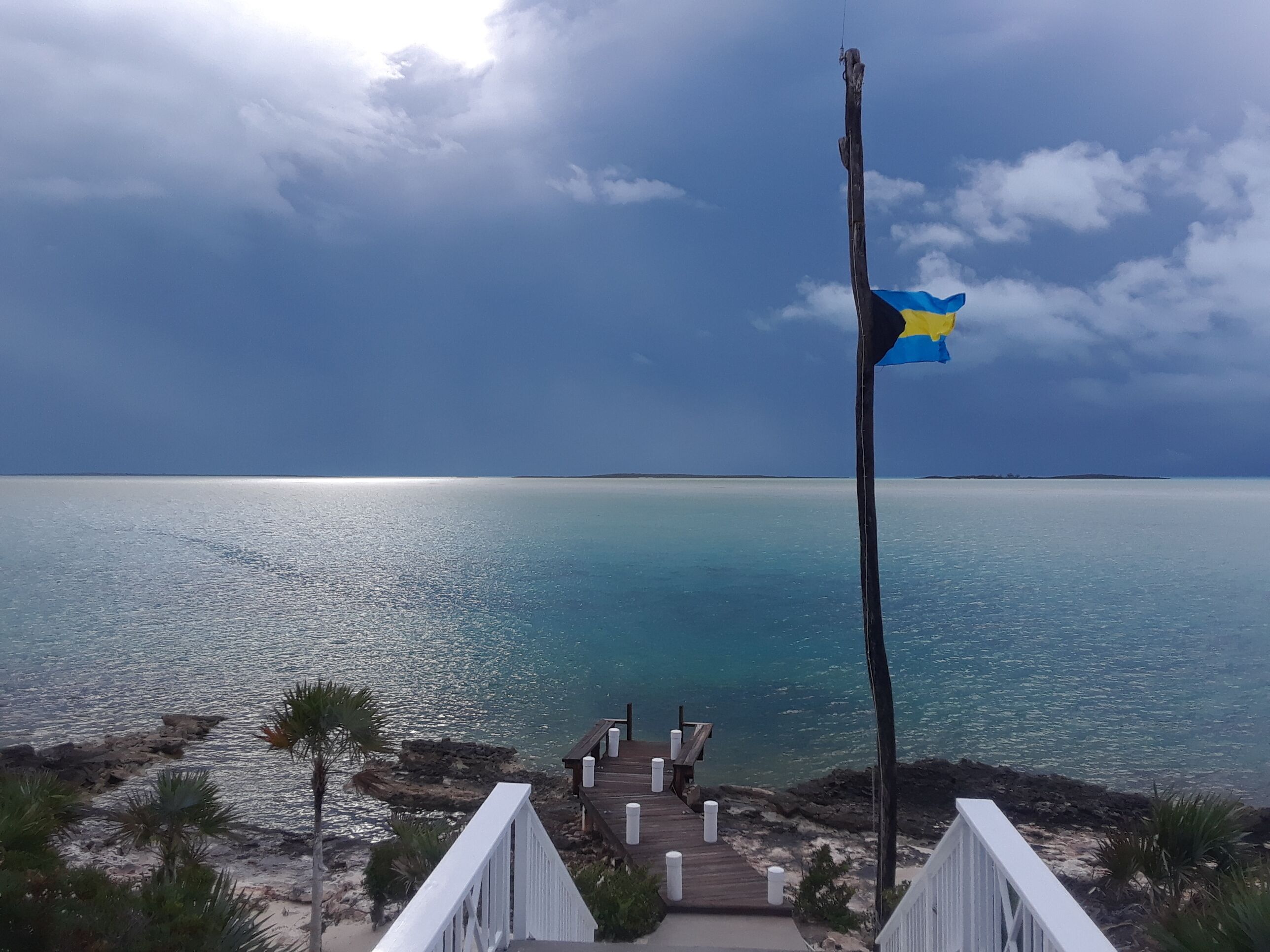 A wooden pier leading to a beach with a flagpole displaying a flag.