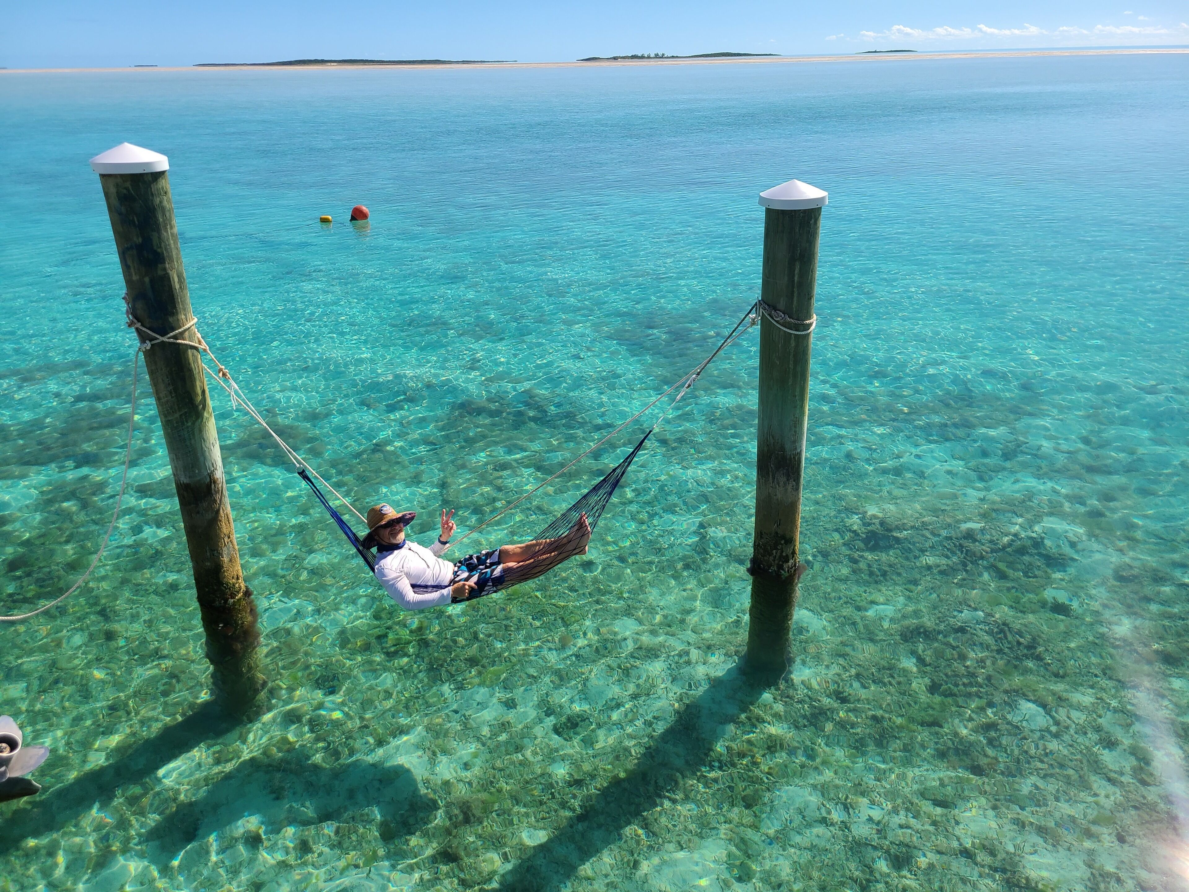 A hammock tied between two posts over clear turquoise water, with a person relaxing in it.