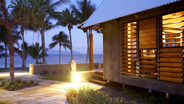 A modern building with a slatted wooden facade, a stone pathway, and palm trees. - Pure Magnetic Villa 1 (Nelly Bay)