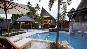 A pool area with lounge chairs, a thatched-roof structure, and a stone wall with a statue. - Pure Magnetic Villa 1 (Nelly Bay)