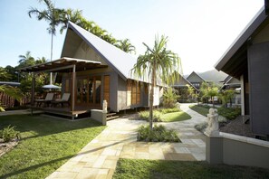 Una villa moderna con patio coperto, vialetto in pietra e un piccolo giardino con palme.