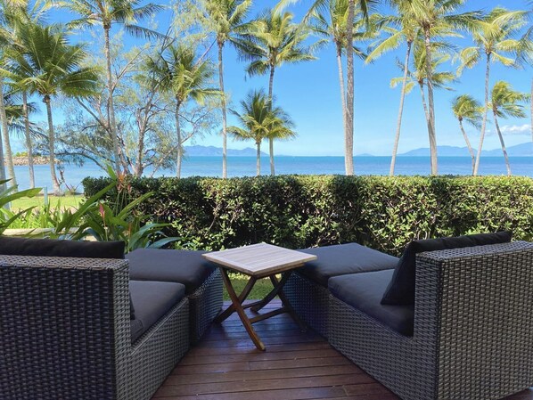Un patio con mobili in vimini, un tavolino e vista sull'oceano e palme.