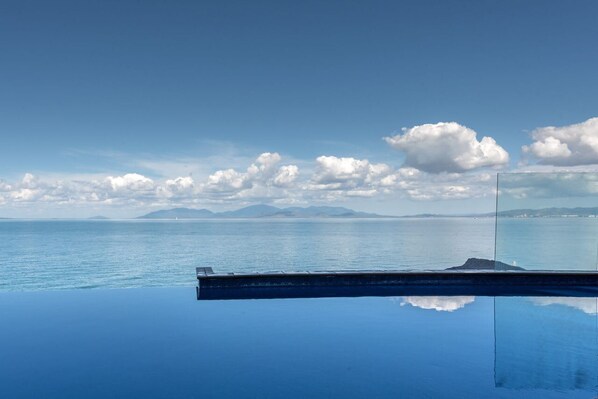 A clear view of the ocean with a distant landmass, a glass barrier reflecting the sky and clouds, and a calm water surface.