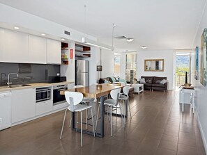 A modern kitchen with white cabinetry, a wooden dining table, and a seating area with a sofa and chairs.