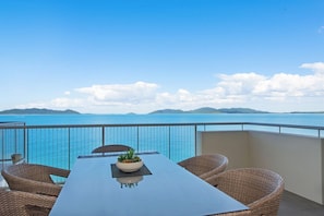 A balcony with a table and chairs, a potted plant, and a view of the sea and distant islands. - 1 Bright Point Apartment 4501 (Nelly Bay)