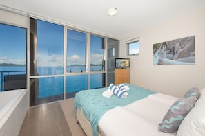 A bedroom with a large window, a bed, a TV, and a painting. - 1 Bright Point Apartment 4501 (Nelly Bay)