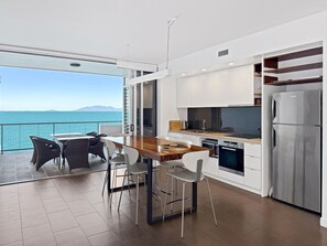 A modern kitchen with a view of the sea, a dining area with chairs, and a large window.