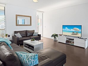 A modern living room with a leather sofa, a coffee table, a TV, and a white entertainment unit.