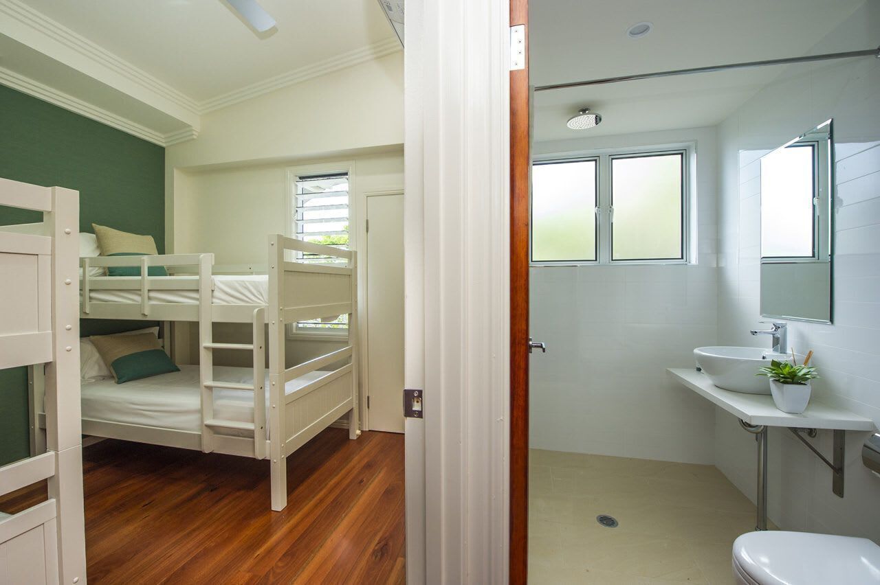 Una habitación con una cama litera, un baño con lavamanos y espejo, y una puerta que da a otra habitación.