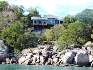 Une propriété située sur la côte, comprenant une grande maison, un rivage rocheux et une végétation luxuriante.