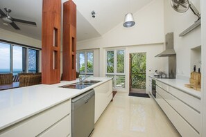 Une cuisine moderne dotée d’un grand îlot central, d’appareils électroménagers intégrés et offrant une vue sur l’extérieur.