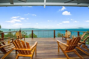 Une terrasse en bois avec des fauteuils Adirondack donnant sur un plan d’eau.