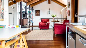 A spacious living area with a high wooden ceiling, a red sofa, a wooden table, and a bookshelf. - Romantic Attic with Superb View of Madonna del Orto Gothic Church (Venezia)