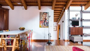 A spacious living area with a wooden ceiling, a dining table with colorful chairs, a red sofa, and a painting on the wall. - Romantic Attic with Superb View of Madonna del Orto Gothic Church (Venezia)