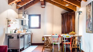 A compact kitchen with wooden beams, a dining area with colorful chairs, and a large window providing natural light. - Romantic Attic with Superb View of Madonna del Orto Gothic Church (Venezia)